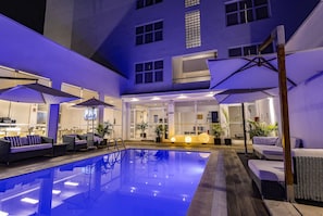 A pool area with lounge chairs and umbrellas, a reception desk, and a building with large windows. - Hotel Gran Palma Piura (Piura)