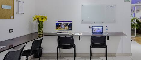 A modern office space with two black chairs, a glass table, a computer, and a whiteboard.