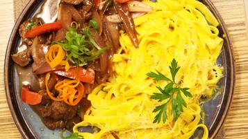 Un plato de fideos amarillos con carne de res y verduras, adornado con perejil.