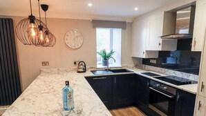 A modern kitchen with a marble countertop, black cabinets, a stainless steel range hood, and a built-in oven. - Leafy Nook (Ambleside)