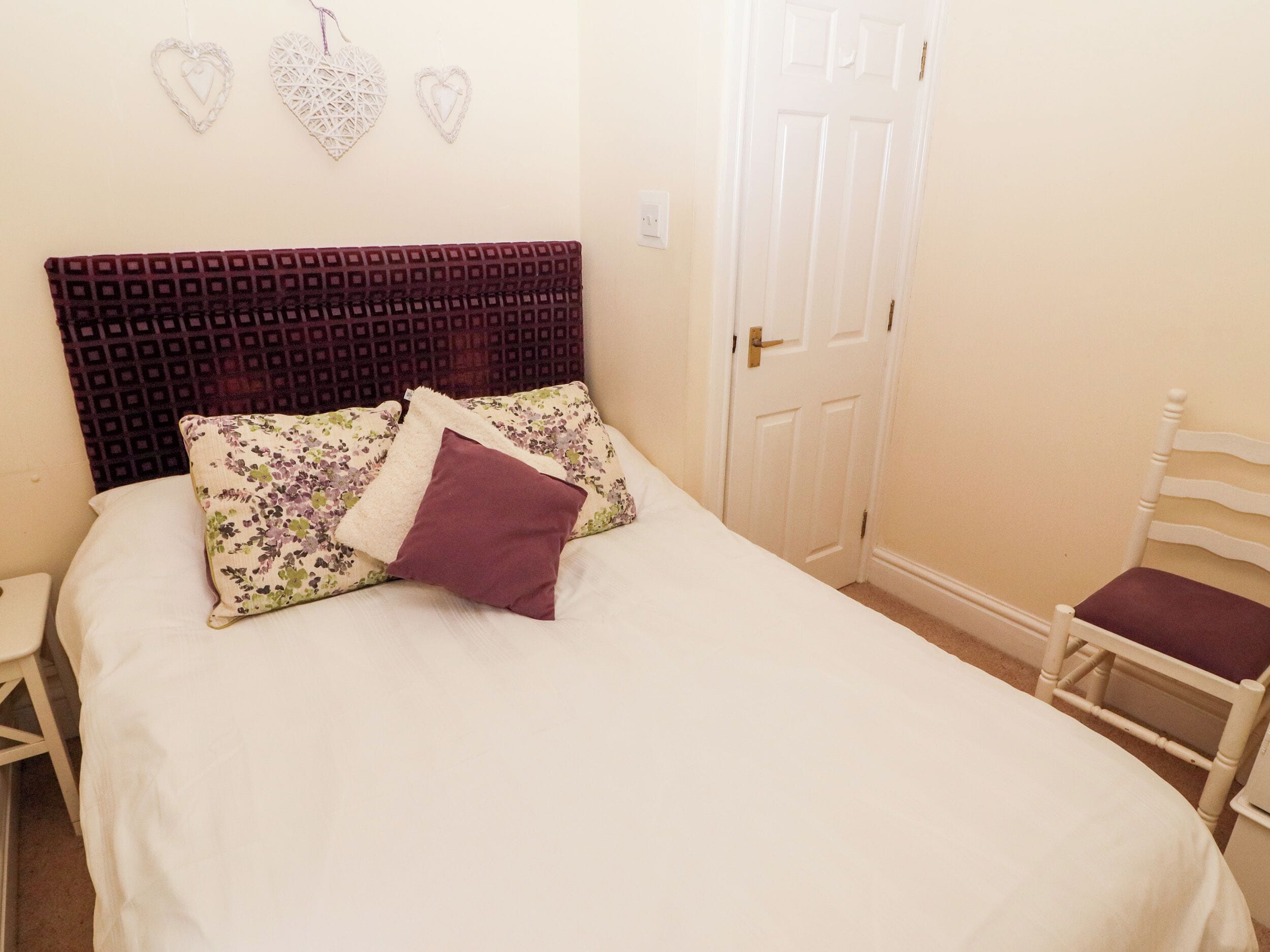 A bedroom with a large bed, a wooden headboard, floral-patterned pillows, and a white door.