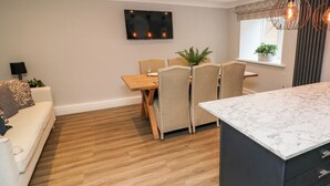 A modern kitchen with a marble countertop, wooden flooring, and a dining area with wicker chairs. - Leafy Nook (Ambleside)