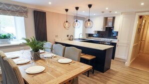 A modern kitchen with a central island, wooden dining table, and bar stools. - Leafy Nook (Ambleside)