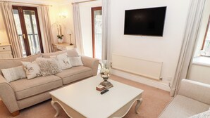A living room with a beige sofa, a white coffee table, and a flat-screen TV mounted on the wall. - Leafy Nook (Ambleside)