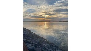 Tyyni ranta, jossa on kivikkoinen rantaviiva ja taustalla auringonlasku.
