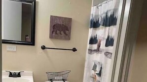 Pieni kylpyhuone, jossa on wc, pesuallas ja peili. Seinällä on karhukuva, ja suihkuverhossa on metsäaihe.