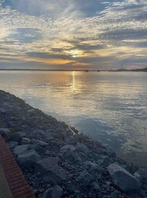 Ruhiges Ufer mit felsigem Ufer und einem Sonnenuntergang im Hintergrund.