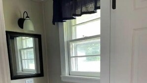 Une petite salle de bain avec un lavabo blanc, un miroir et une fenêtre agrémentée d’une lambrequin noire.