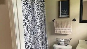Une salle de bain avec un rideau de douche à motifs, des toilettes, un porte-serviettes avec une serviette et une citation encadrée accrochée au mur.