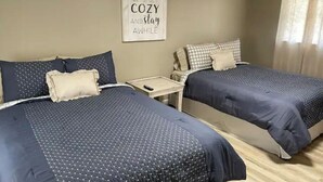 Une chambre d’hôtel avec deux lits, chacun recouvert d’une couvre-lit bleu foncé et agrémenté d’oreillers assortis. Une petite table avec une télécommande se trouve entre les deux lits.