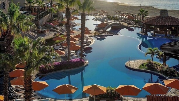 A resort pool area with multiple lounge chairs and umbrellas, surrounded by palm trees and a view of the beach. - Room with a view of the Pacific and a private Jacuzzi at Sunset Beach Resort (Cabo San Lucas)