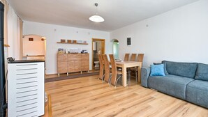 Una sala moderna con una mesa de comedor de madera, un sofá gris y una cocina con un mueble de madera y una lámpara colgante.