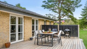 Eine Terrasse mit Tisch, Stühlen, einem Grill und einer Ziegelwand mit großen Fenstern.