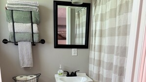 A bathroom with a toilet, sink, and a mirror above the sink. There is a towel rack with towels and a basket of toiletries on the toilet. - Motel at KY Lake. Reel & Relax (Gilbertsville)