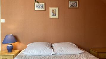 Une chambre à coucher avec un lit, deux oreillers, une table de chevet avec une lampe et trois tableaux encadrés accrochés au mur.