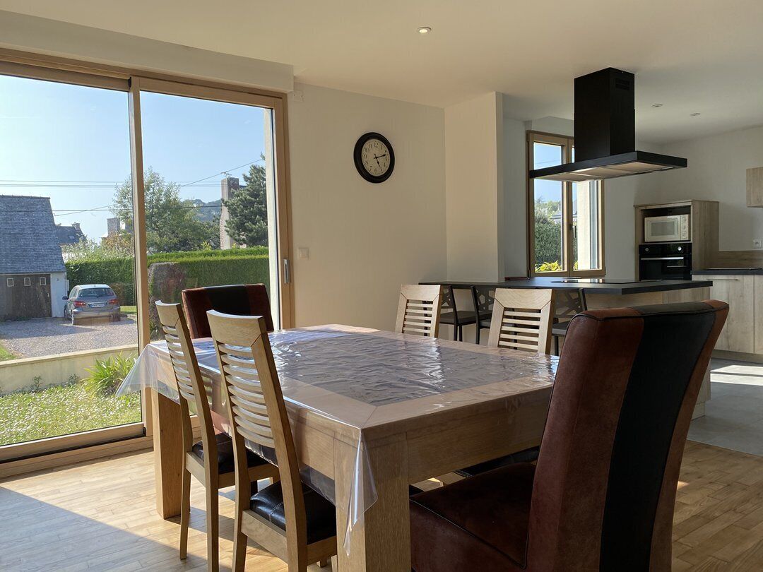 Uma sala de jantar moderna com uma mesa grande e cadeiras, uma cozinha com micro-ondas e forno, e vista para o exterior.