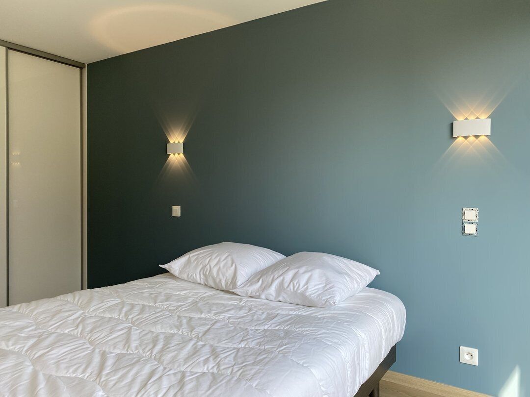 A bedroom with a bed, two wall-mounted light fixtures, and a door.
