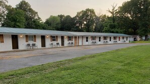 A row of motel rooms with individual doorways, a covered parking area, and a grassy lawn.