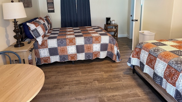A hotel room with two beds, a wooden ceiling, a TV, an air conditioner, and a small table with a lamp.