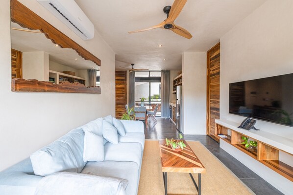 Un salon moderne avec un canapé, une table basse et un téléviseur. On y trouve également un ventilateur de plafond et un appareil de climatisation.