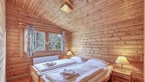 Quarto de cabana de madeira com duas camas, uma janela com cortinas e um radiador.