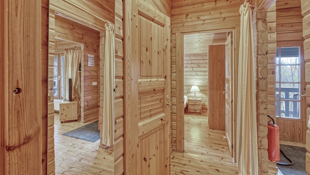 Interior de uma cabana de madeira, com um corredor que dá para um quarto, um banheiro pequeno e uma janela com vista.