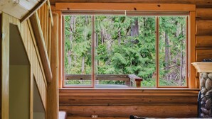 Ein Holzblockhaus-Interieur mit einem großen Fenster, einer Treppe und einer gemütlichen Sitzecke.