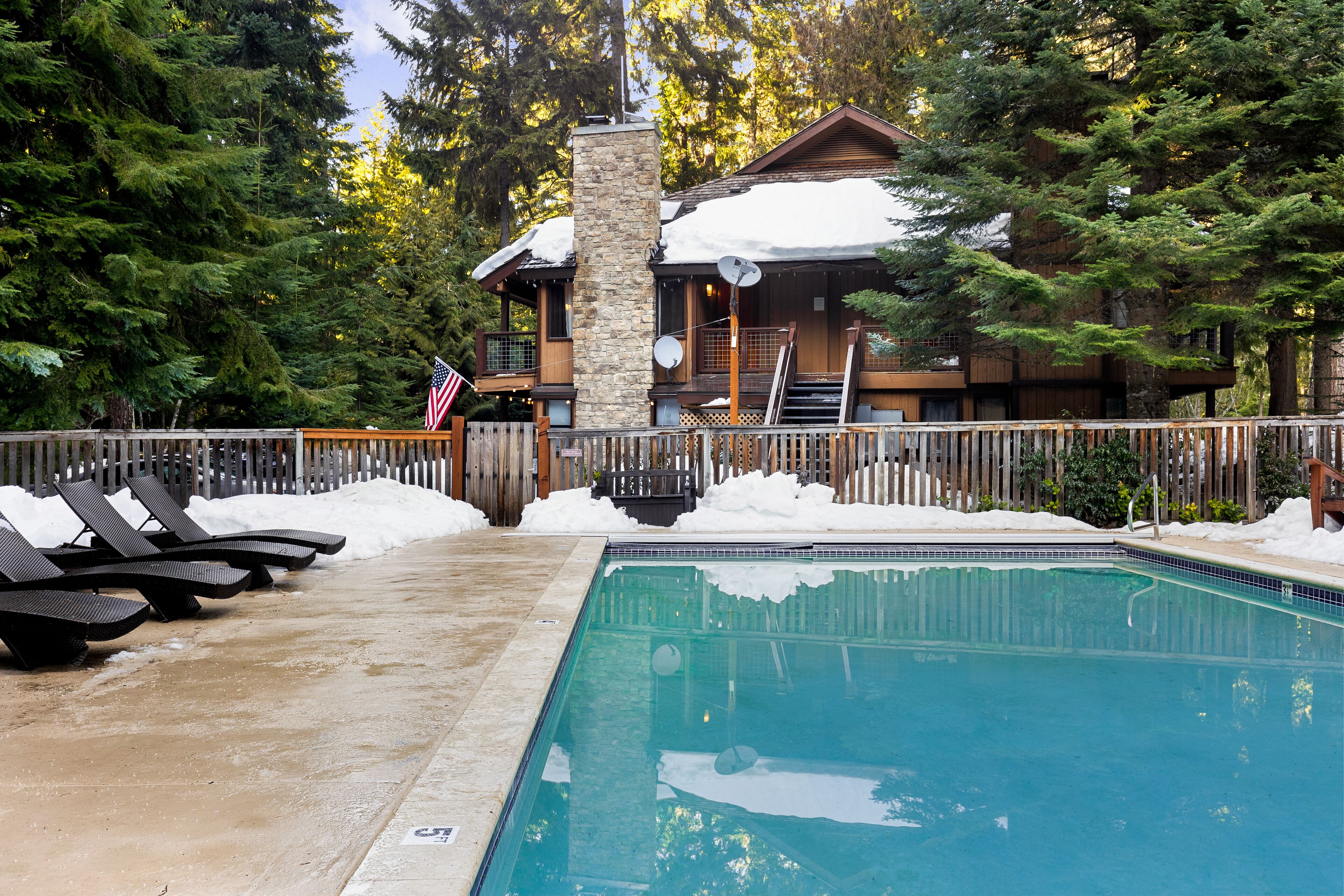 Un espace piscine avec des chaises longues, un pilier en pierre et un bâtiment en bois dont le toit est recouvert de neige.