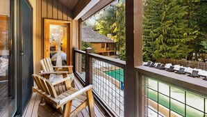 Eine Holzterrasse mit Stühlen, einer Glastür und Blick auf ein Schwimmbad und Bäume.