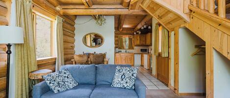 L’intérieur d’une cabane en rondins, avec un canapé, une table basse, une table à manger et un coin cuisine.