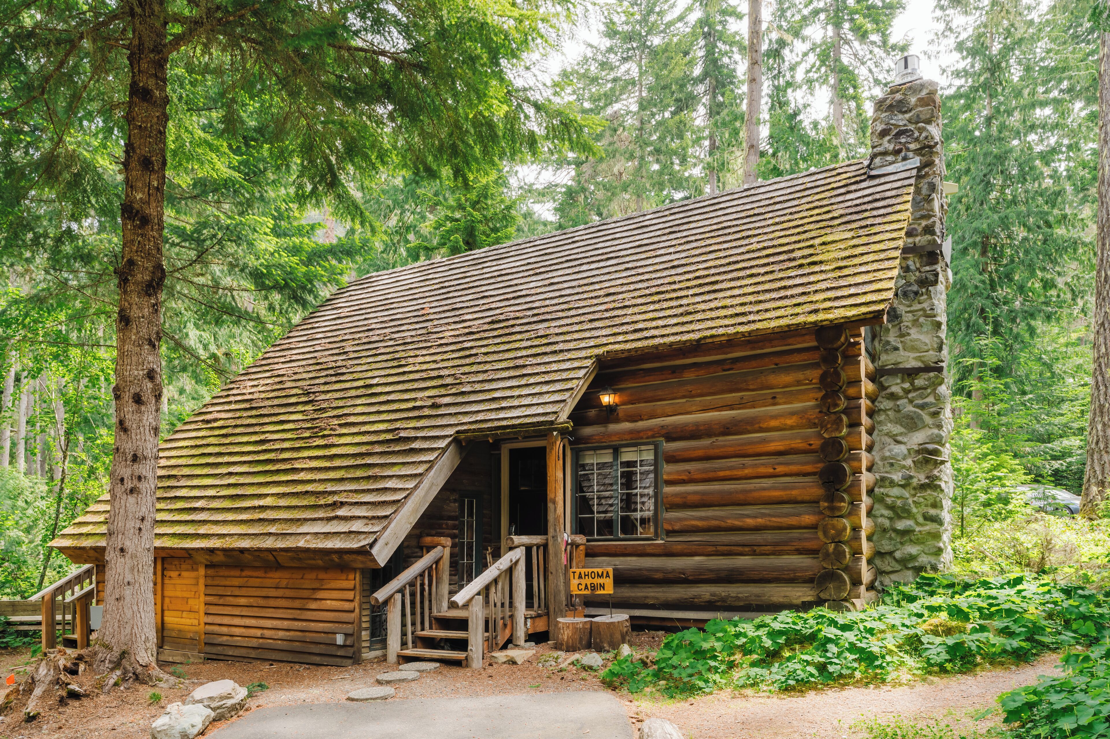 A rustic log cabin with a stone chimney, wooden stairs, and a sign indicating it is the Tahoma Cabin.