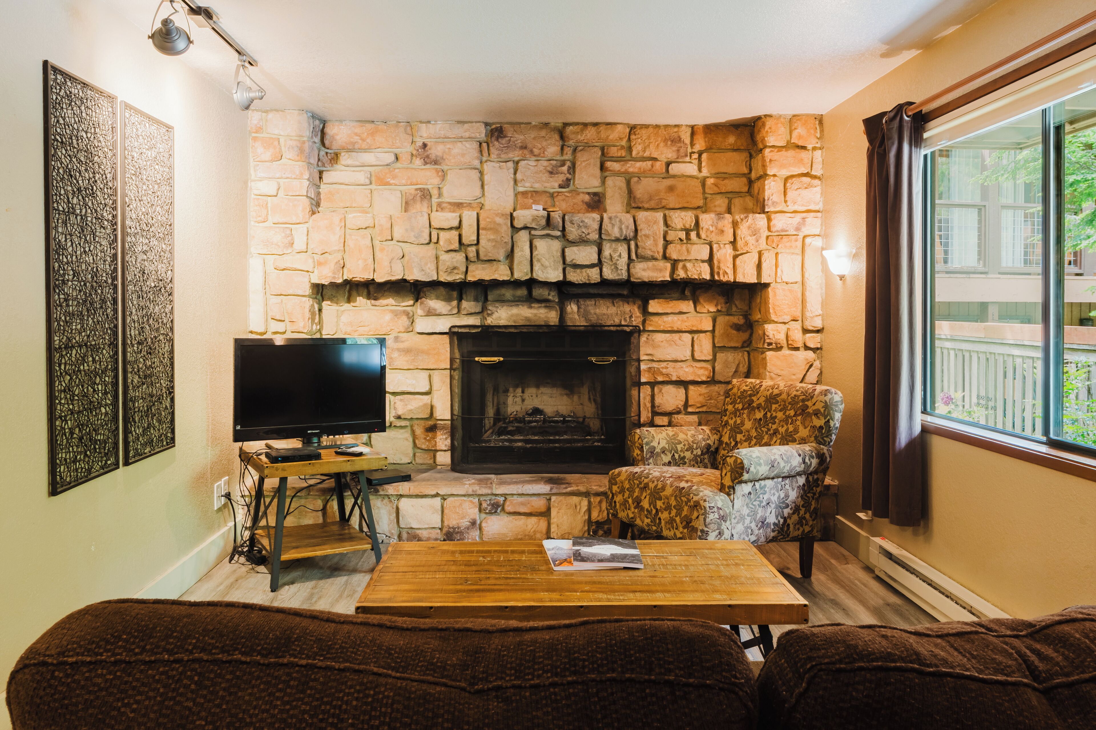 Una sala de estar acogedora con chimenea de piedra, un televisor, un sillón estampado y una mesa de centro de madera.