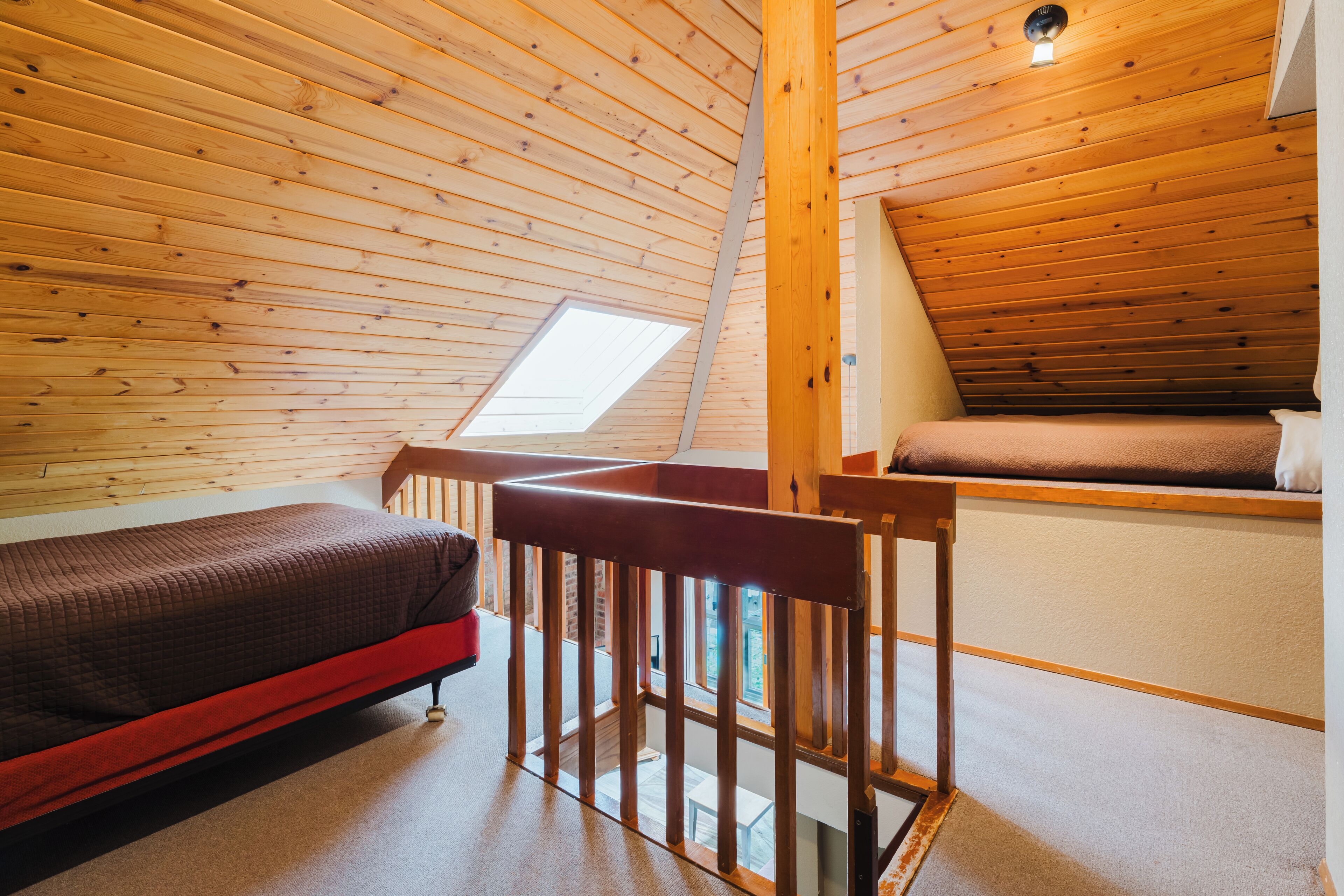 Una habitación pequeña y acogedora con techo inclinado, una cama individual, otra litera y un tragaluz.