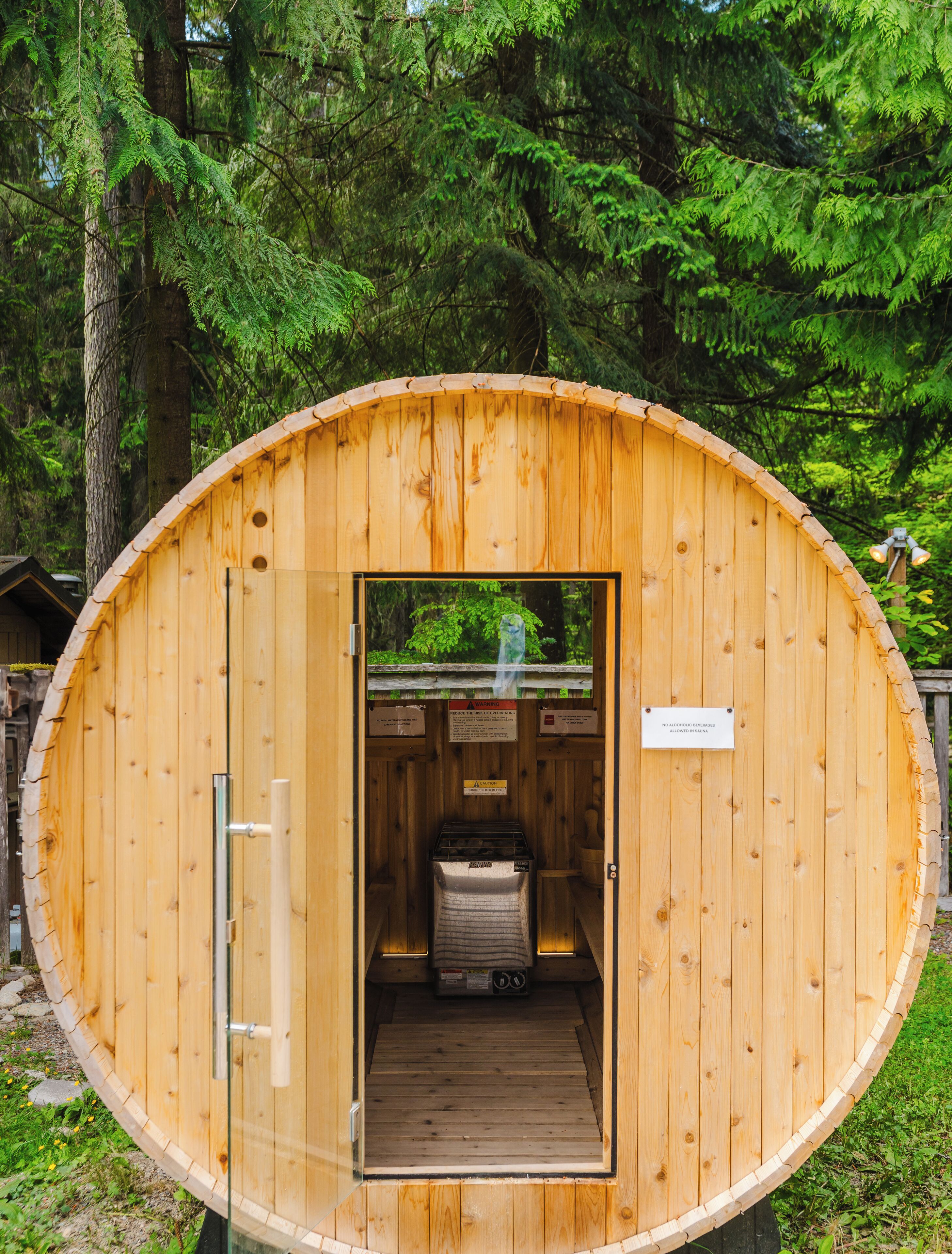 A wooden sauna structure with a glass door, a bench inside, and a sign indicating no alcoholic beverages allowed.