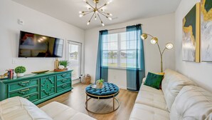 A modern living room with a sofa, a round ottoman, a television, a green cabinet, and a ceiling light fixture.