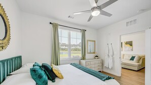 A bedroom with a bed, a ceiling fan, a window with curtains, a dresser, a mirror, and a view of the outside.