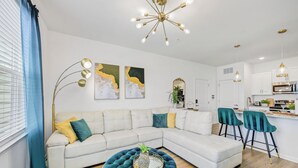 A modern living room with a sectional sofa, a round ottoman, and a kitchen area with bar stools.