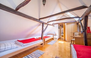 Une chambre confortable située sous les combles, avec des poutres apparentes, deux lits simples, une petite table et une armoire.