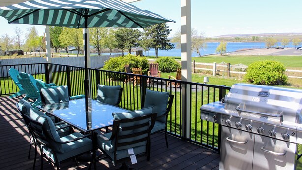Une terrasse extérieure couverte, équipée d’une table et de chaises, d’un barbecue et offrant une vue sur un lac.