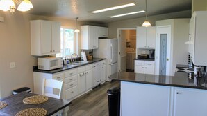 Une cuisine moderne avec des meubles blancs, un plan de travail noir et un coin repas doté d’une table en bois.