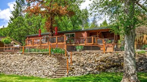 A log cabin with a deck, outdoor seating, and a stone staircase. - 'RIVER HAVEN' is a serene riverside cabin on the Rogue River (Trail)