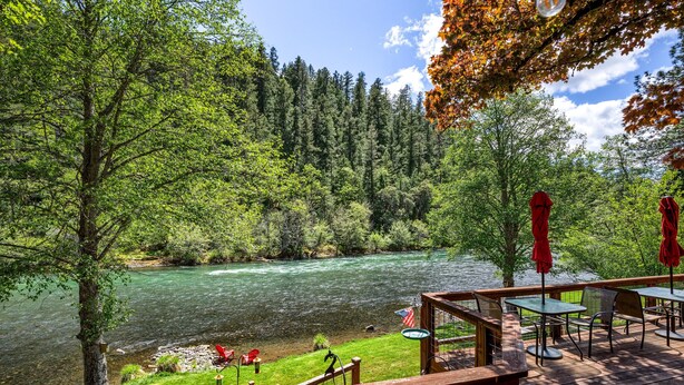A deck with outdoor seating overlooking a river, surrounded by trees. - 'RIVER HAVEN' is a serene riverside cabin on the Rogue River (Trail)