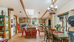 A spacious kitchen with wooden beams, a central island with stools, and a dining area with a table and chairs. - 'RIVER HAVEN' is a serene riverside cabin on the Rogue River (Trail)