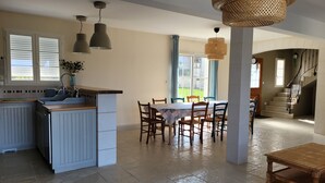 Een ruime keuken met een centraal eiland, een eethoek met tafel en stoelen, en een trap naar een bovenverdieping.