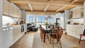 A spacious kitchen with wooden beams, large windows, and a dining area with a view of the water. - Amazing home in Frøstrup with sauna (Frøstrup)