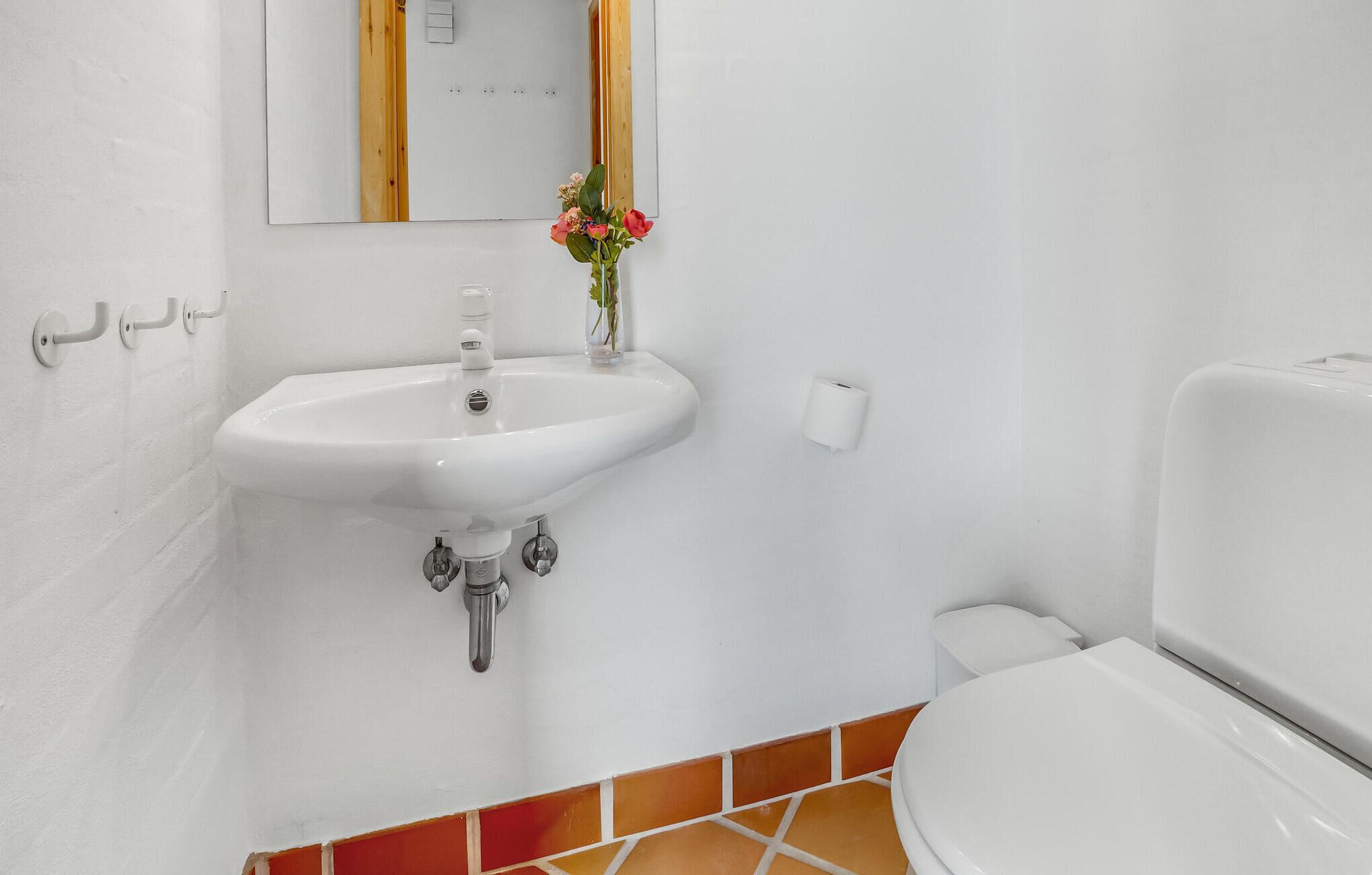 Une salle de bain avec un lavabo blanc, un miroir, des toilettes et un petit vase avec des fleurs.