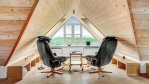 An attic room with a sloped ceiling, two black leather chairs, a small round table, and a window with a view of green hills. - Amazing home in Frøstrup with sauna (Frøstrup)