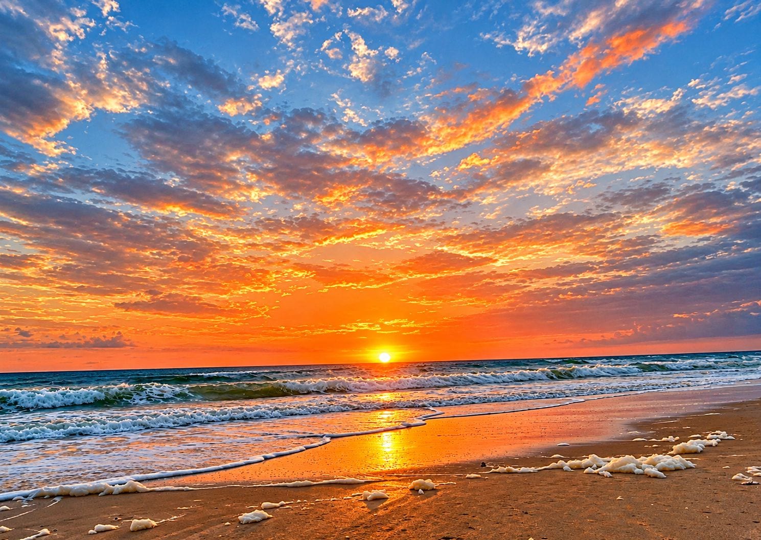 A beach with waves at sunset, a clear sky, and a visible horizon.