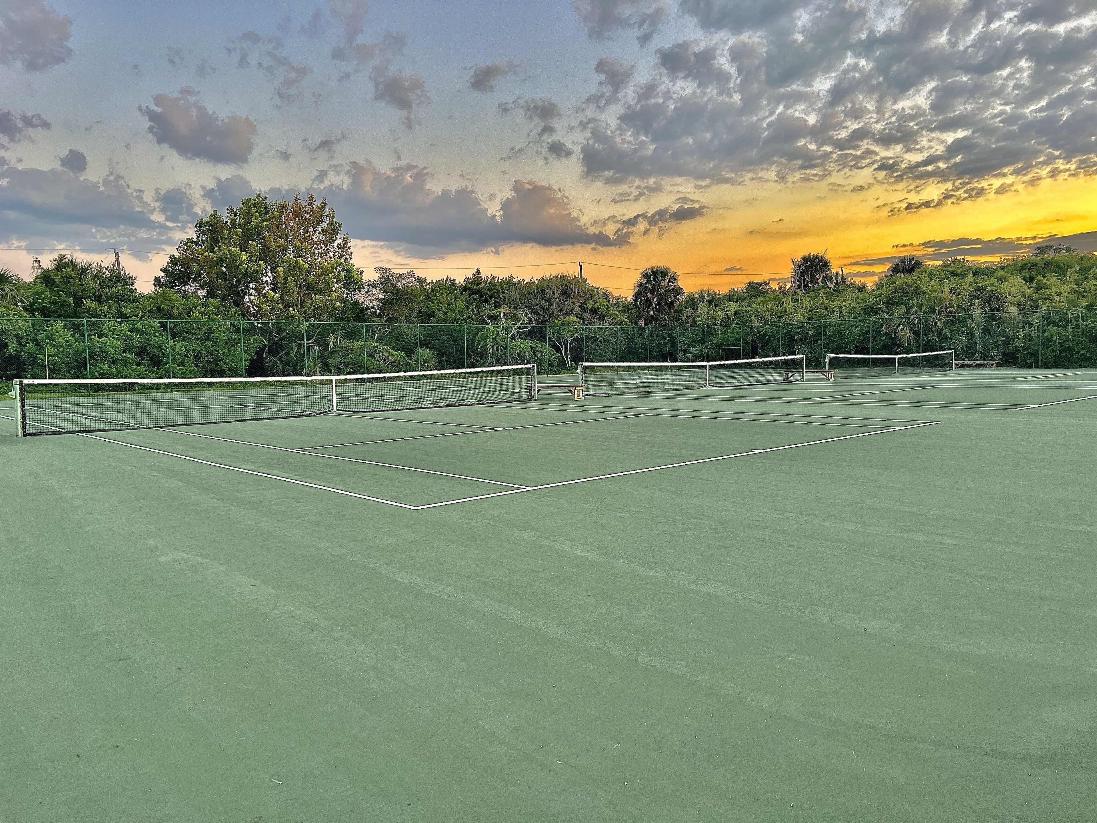 Una cancha de tenis con red, rodeada de árboles y un cielo al atardecer.