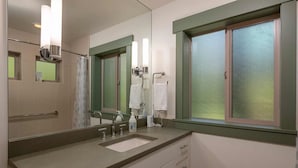 A bathroom with a large mirror, a sink, a shower, and a window with frosted glass.